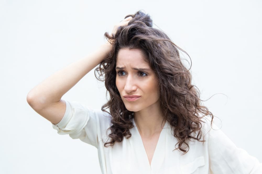 Mujer de pelo oscuro rascandose la cabeza