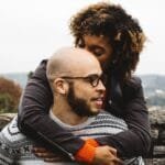 Un señor con alopecia androgénetica siendo abrazado por la esposa.